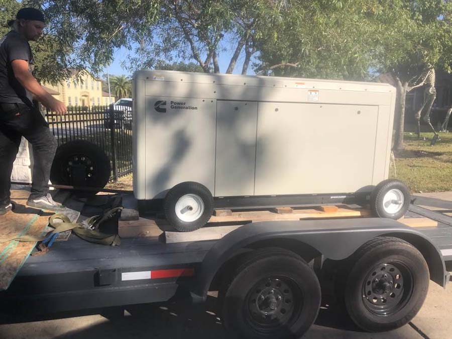Man loading a large, beige Cummins generator onto a trailer.