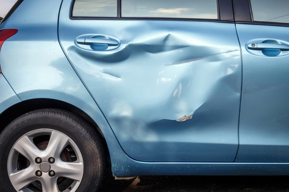 A Light Blue Car With a Severely Dented Rear Door, Showcasing Significant Damage