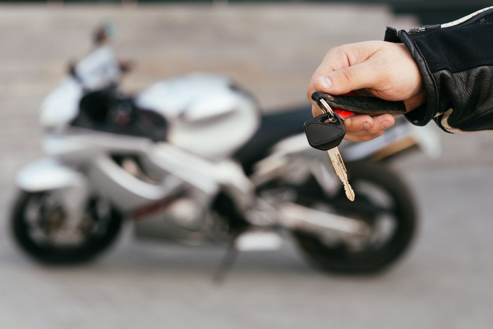 Hand Holding Motorcycle Keys in Front of a Silver Sport Bike — All Pro Locksmiths In Port Macquarie, NSW