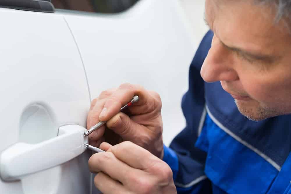 Man Using Lock Picks on a White Car Door Handle — All Pro Locksmiths In Port Macquarie, NSW