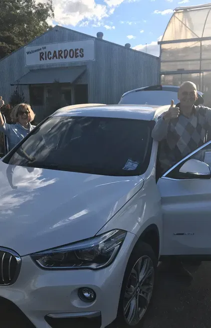 Man Giving Thumbs Up Next to White BMW SUV at Ricardoe's Market — All Pro Locksmiths In Port Macquarie, NSW