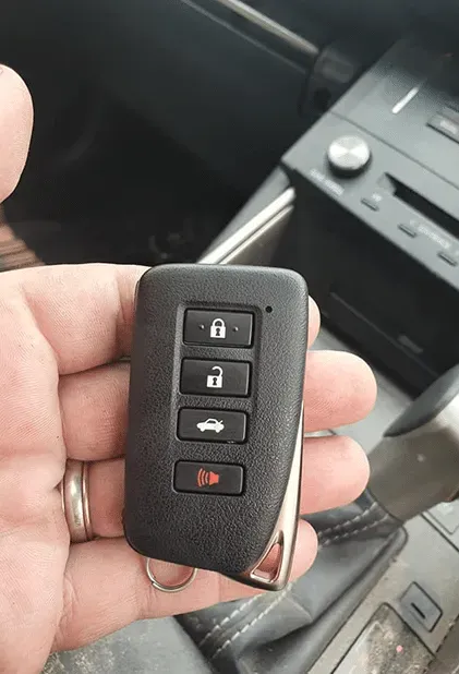 Person Holding a Black Car Key Fob With Four Buttons and a Silver Trim — All Pro Locksmiths In Port Macquarie, NSW