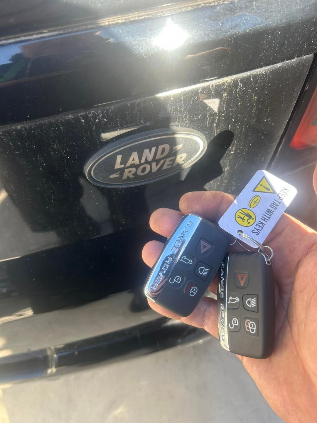 Hand holding car keys in front of a black Land Rover logo on a vehicle. — All Pro Locksmiths In Port Macquarie, NSW