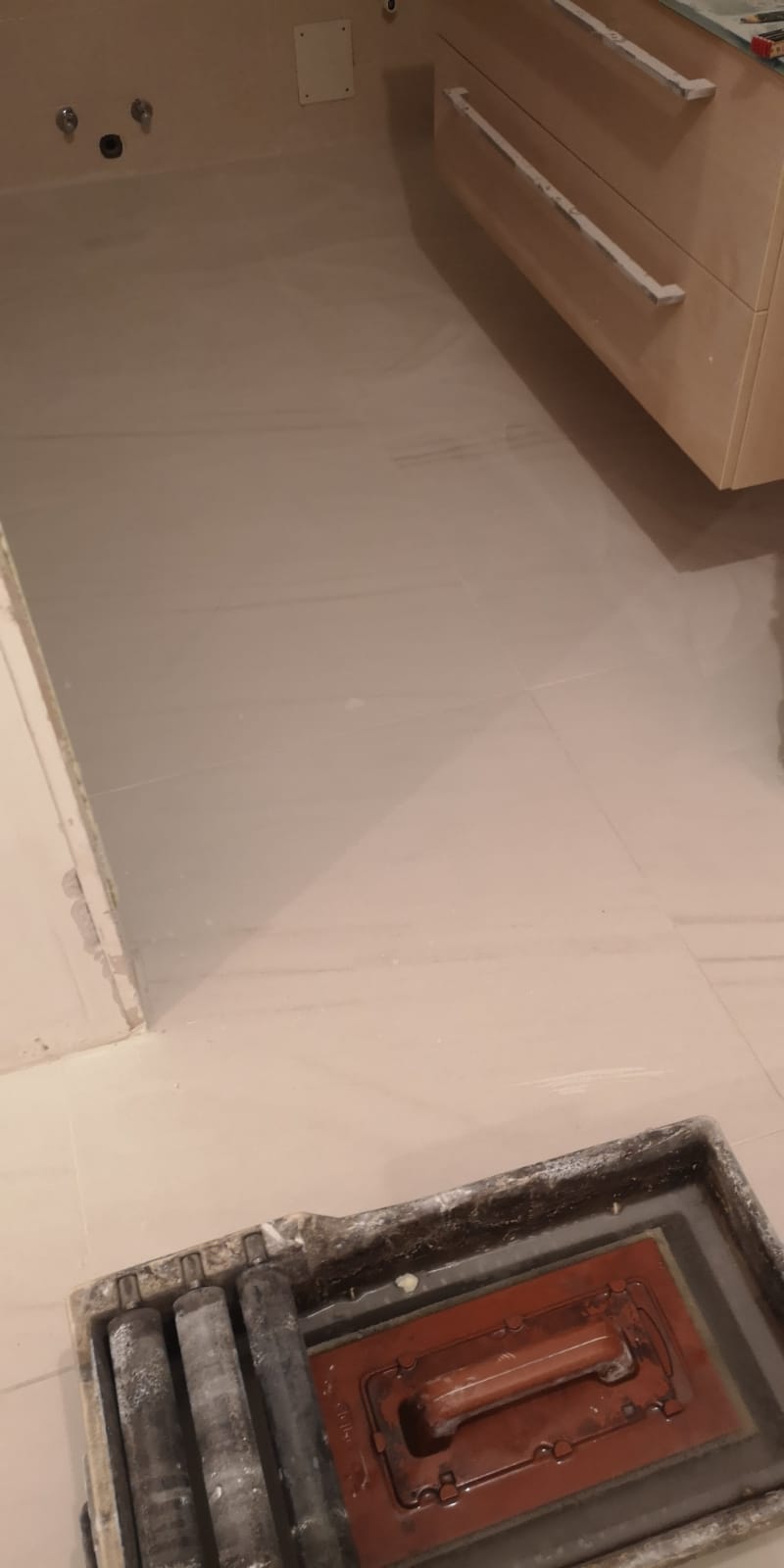 Un tombino è appoggiato sul pavimento di un bagno, accanto a un lavandino.