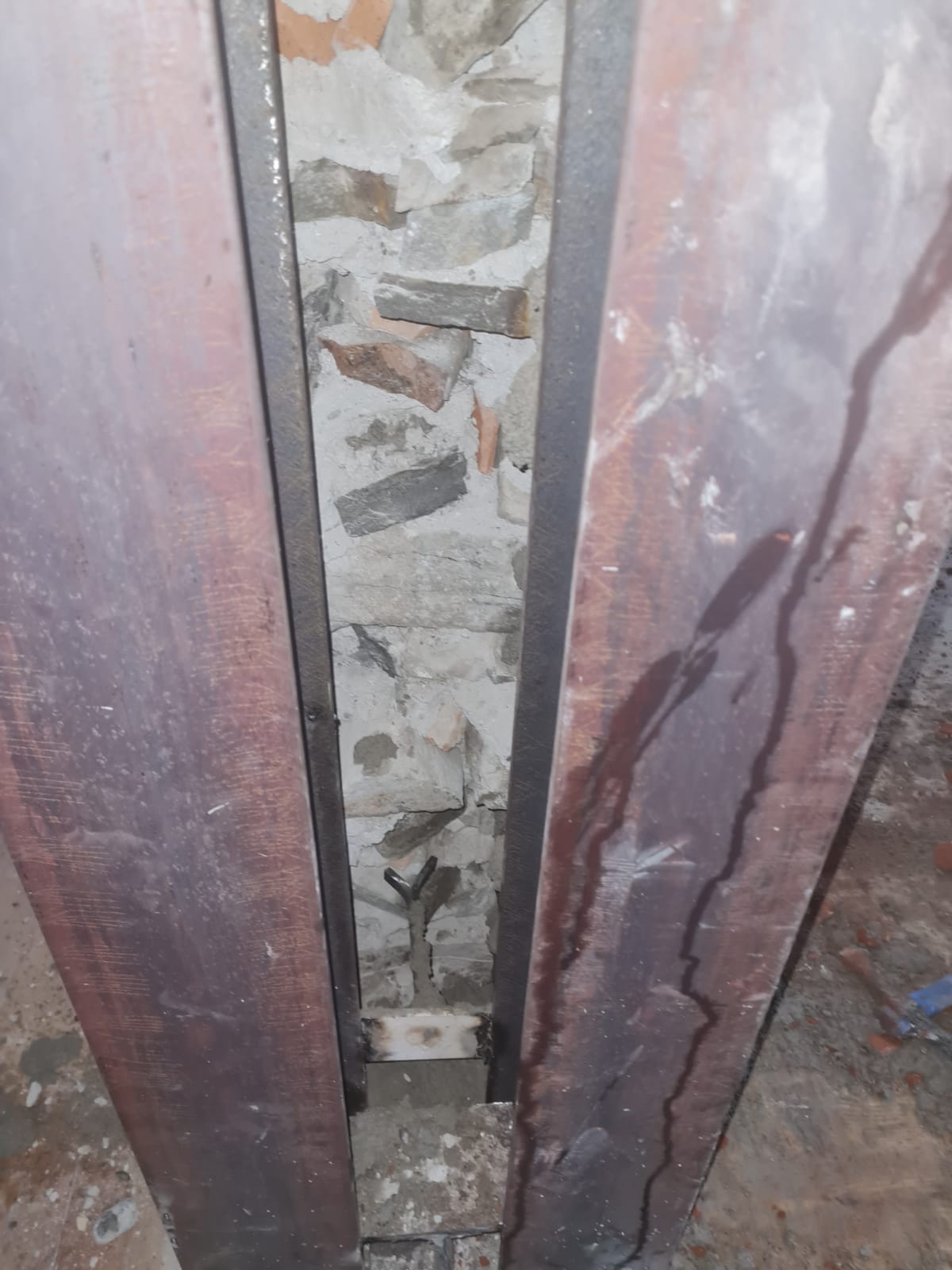 Un muro di mattoni con una trave metallica tra i mattoni.