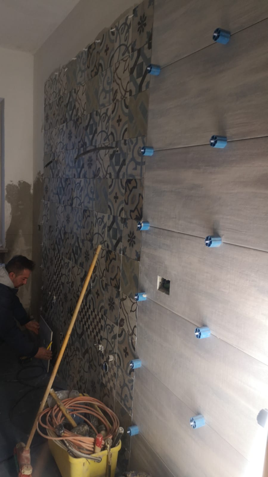 Un uomo sta posando le piastrelle su un muro in un bagno.