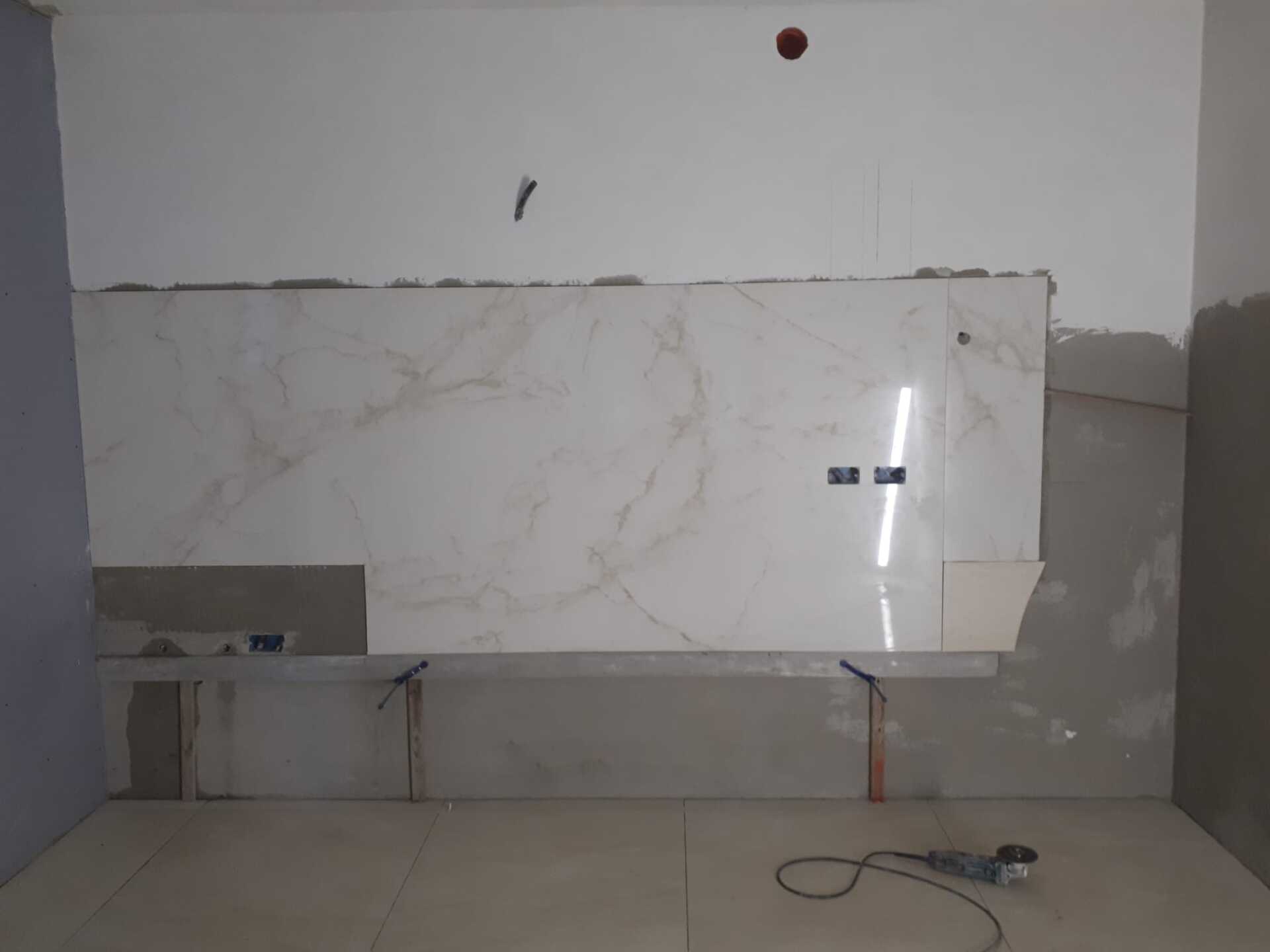 Una stanza con una grande parete piastrellata bianca e un trapano sul pavimento.