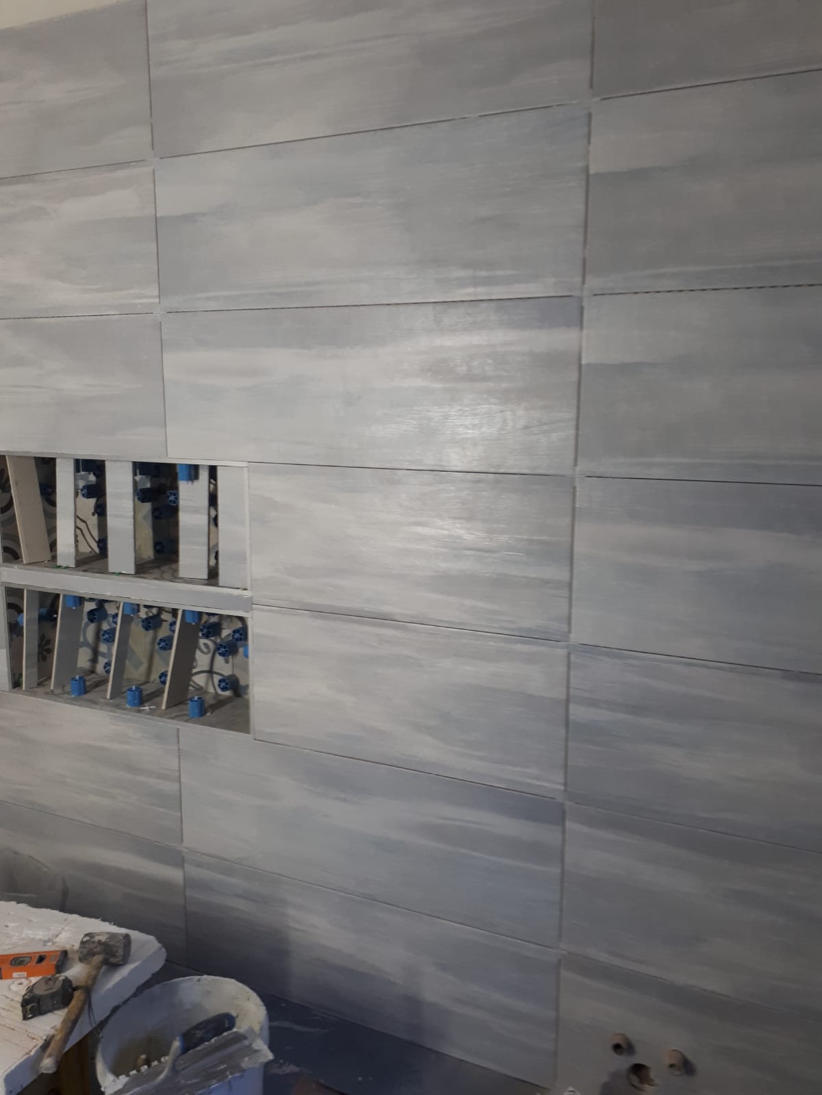 Un bagno con una parete piastrellata grigia e un lavandino.