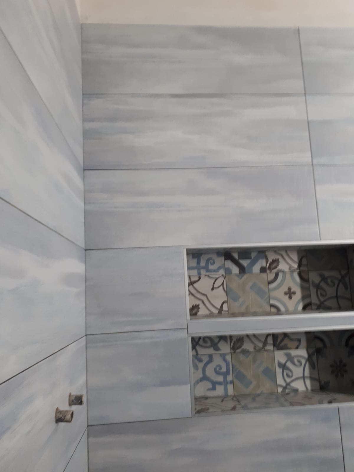 Un bagno con piastrelle grigie e una mensola nell'angolo.