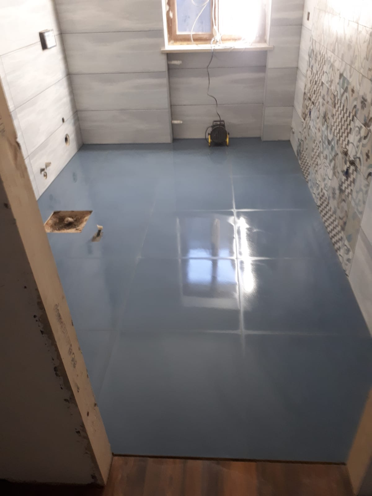 Un bagno con pavimento in piastrelle blu e una finestra.