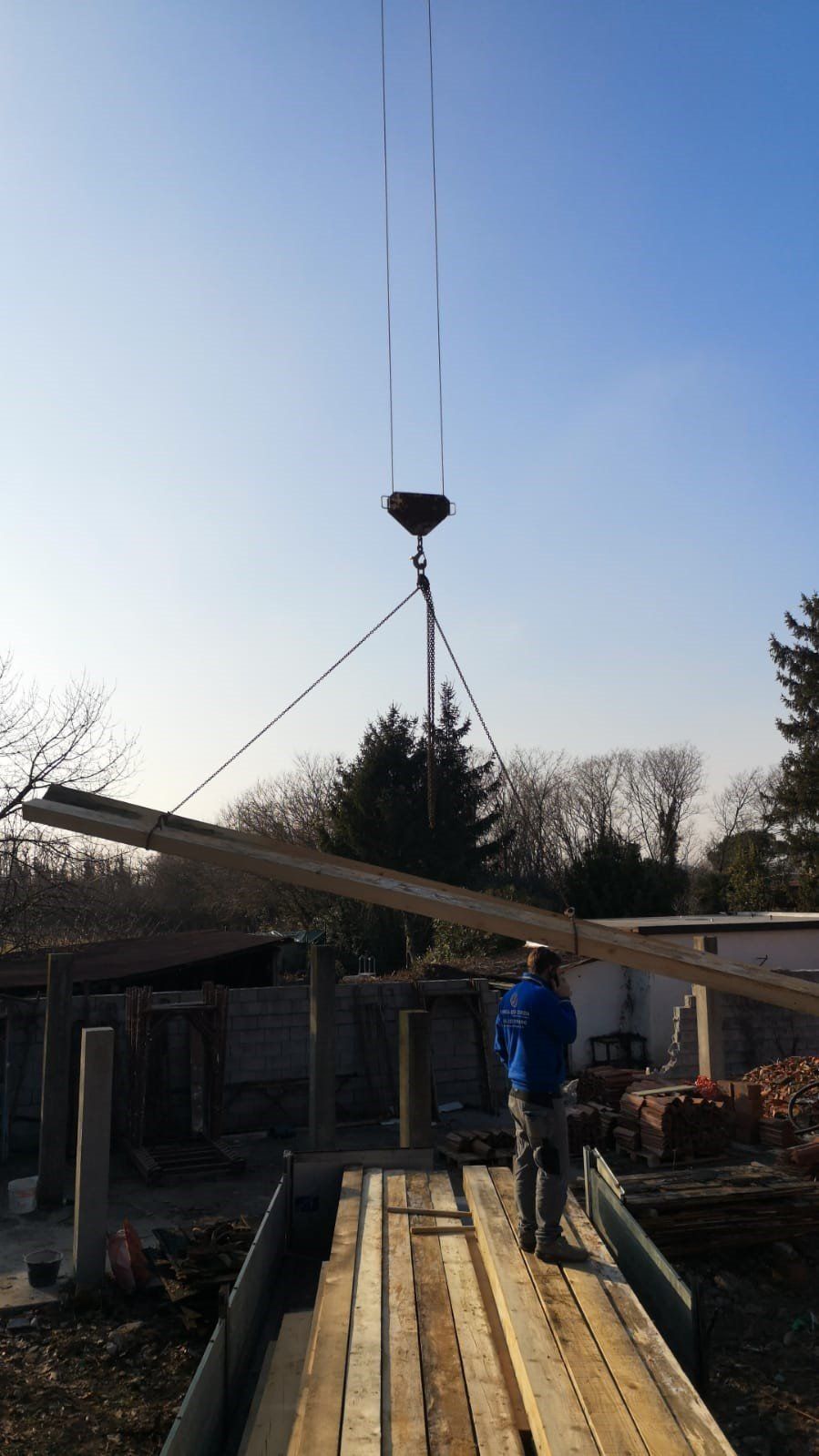 Un uomo è in piedi su una piattaforma di legno mentre una gru solleva un grosso pezzo di legno.