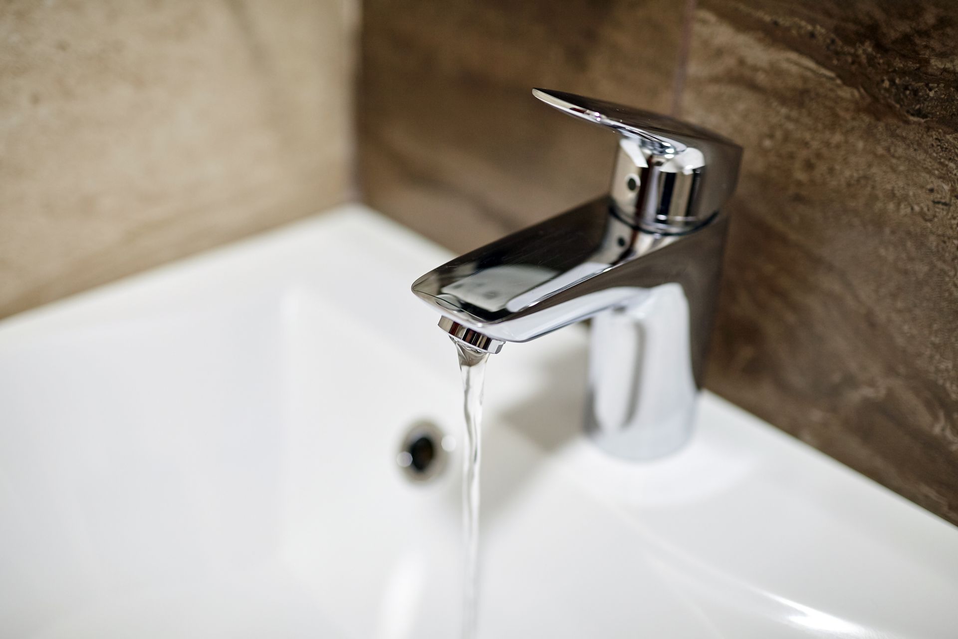 Chrome faucet over a white sink, with water running.