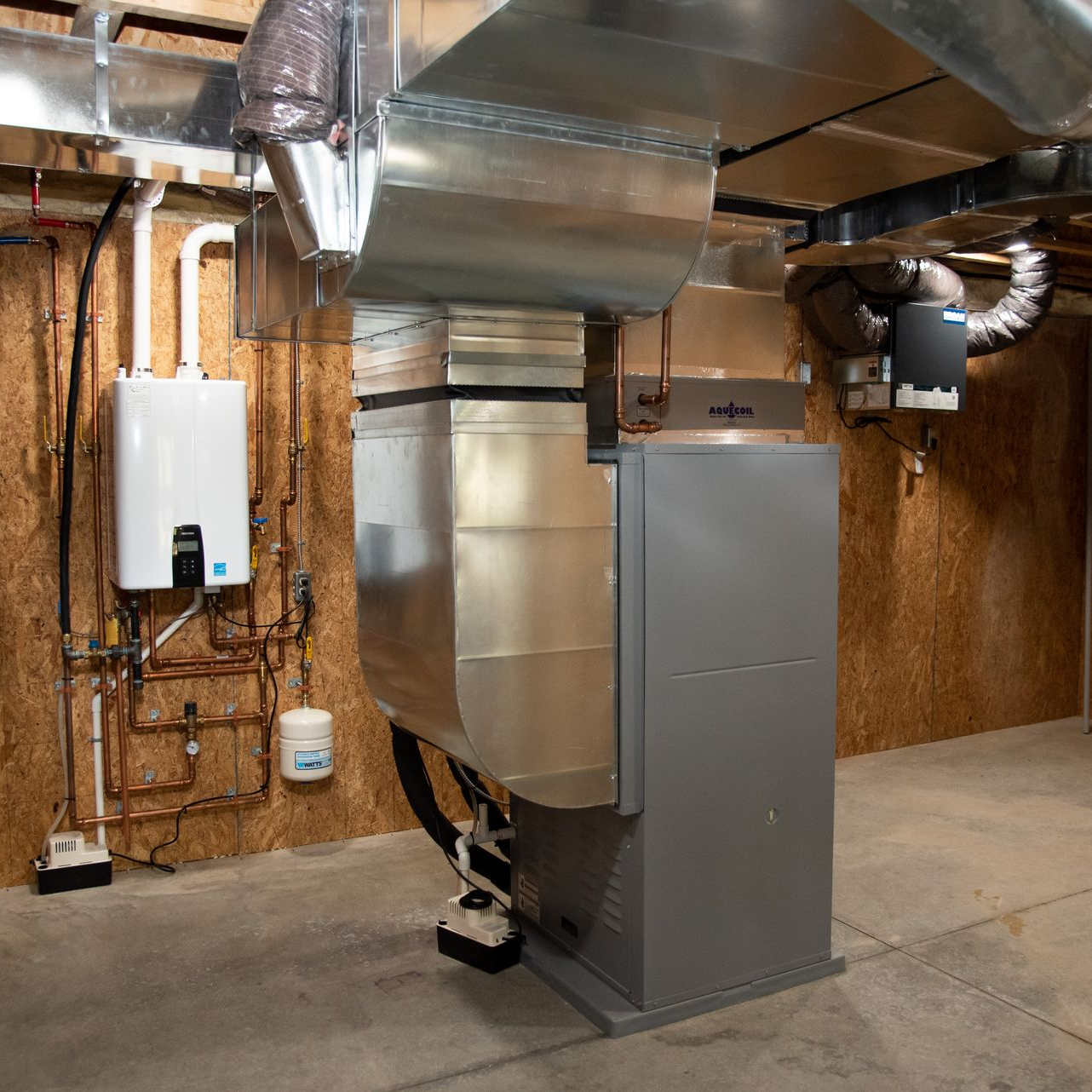 A white Bosch air source heat pump unit sits on a concrete pad in a garden next to a dark stone wall and flower boxes.