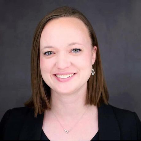 A woman wearing a black jacket and a necklace is smiling for the camera.