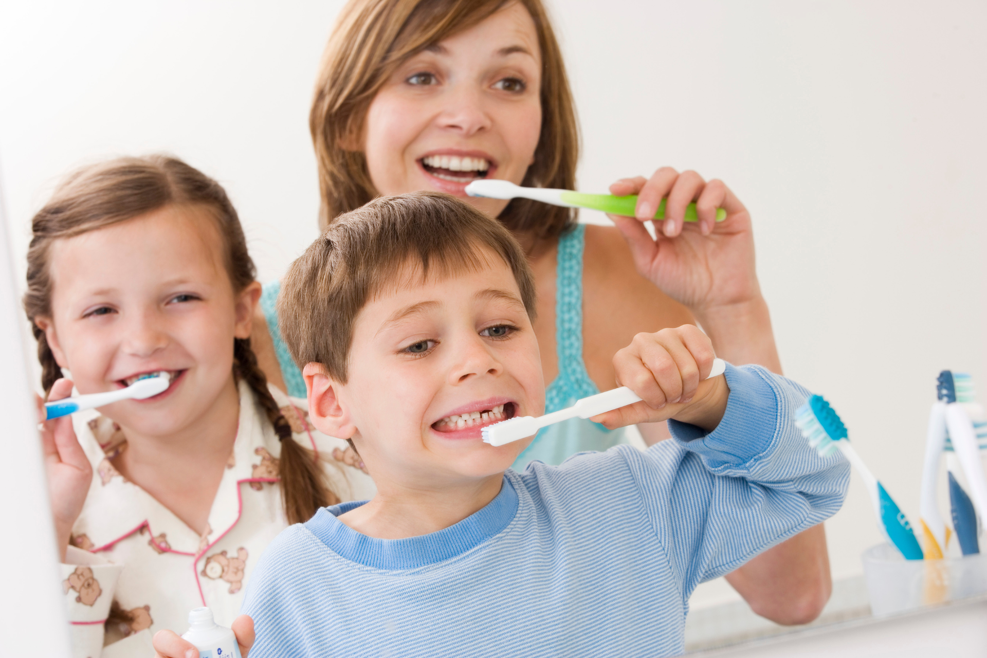 Woman and two children brushing teeth in bathroom.