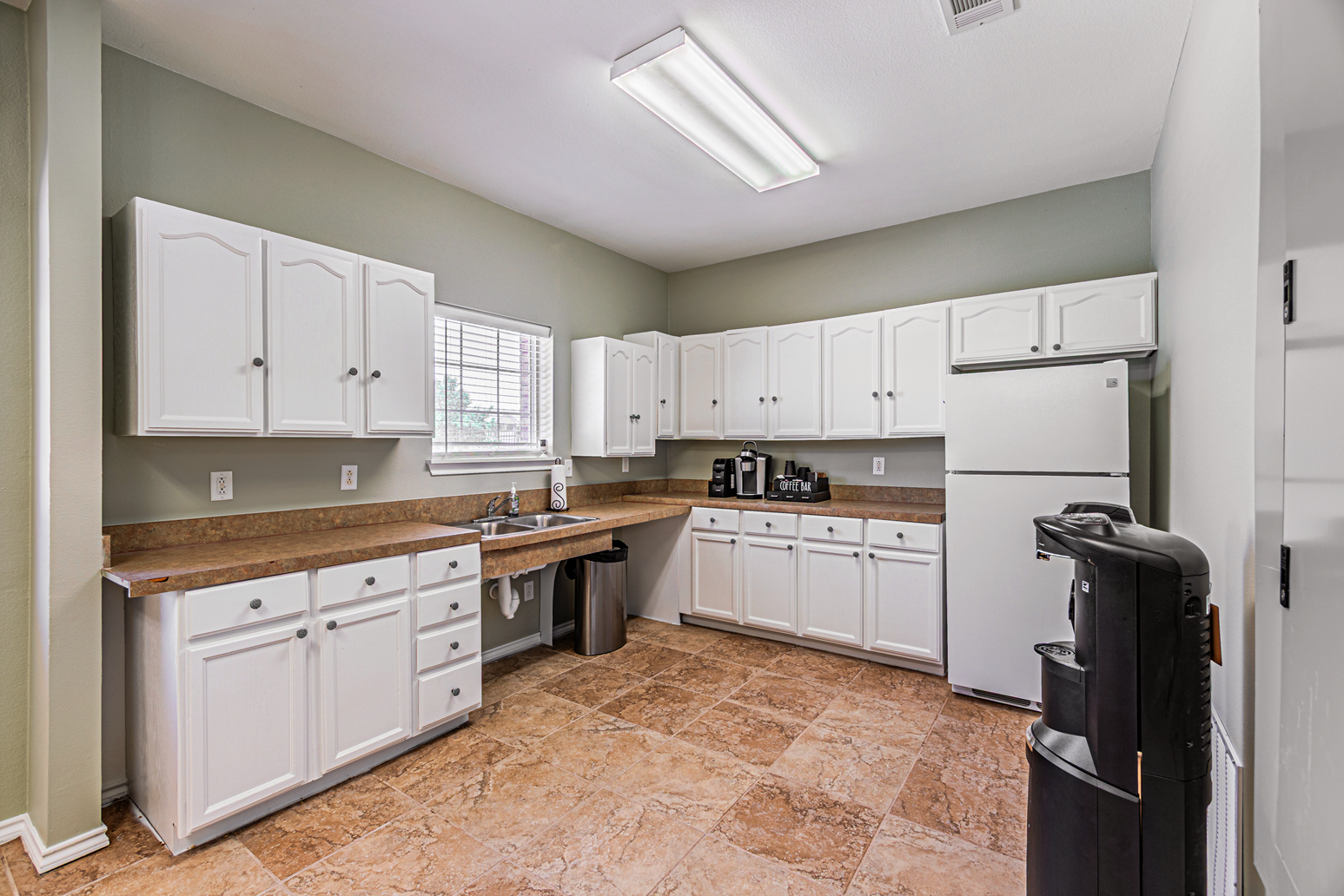 Bright kitchen with white cabinets, wood countertops, stainless stove, and refrigerator on a cork floor.