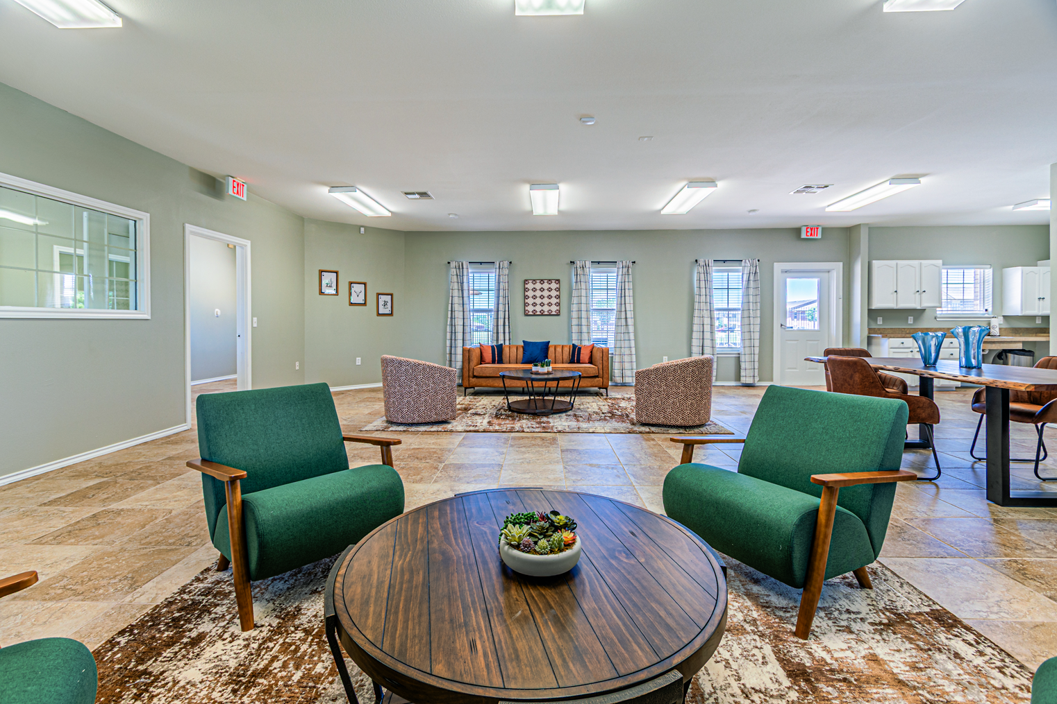 Bright lounge with green chairs, round table, patterned rug, and seating area in a modern lobby