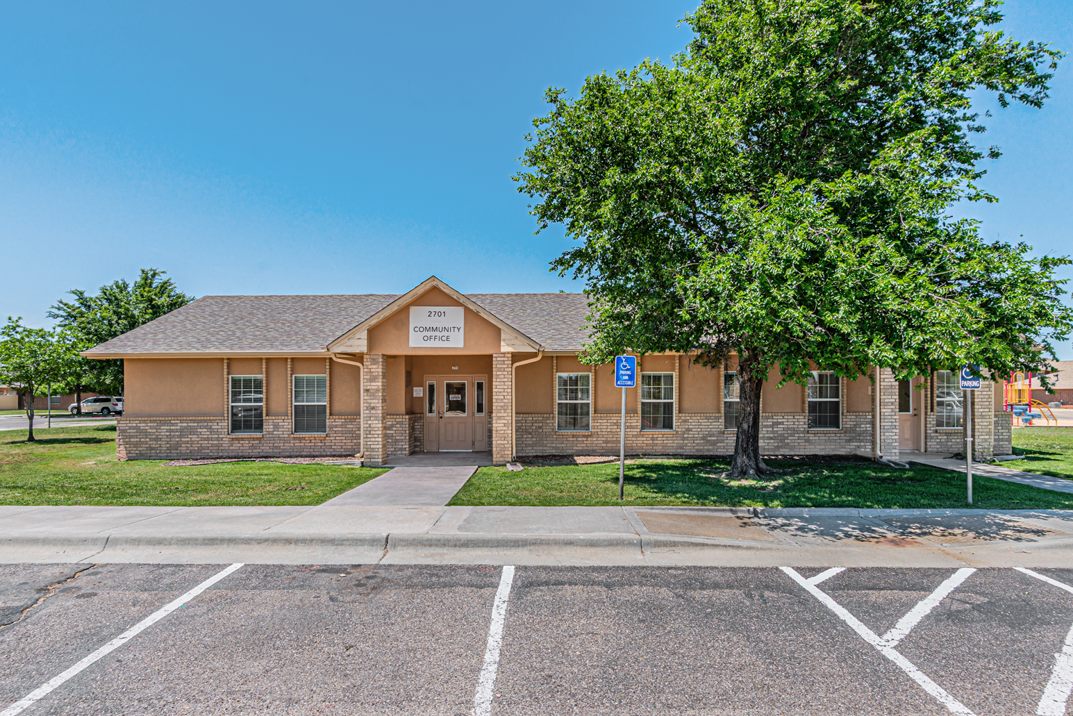 Single-story brick building with a central entrance, trees, and a parking lot in front