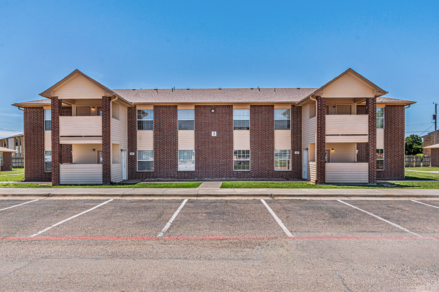 Two-story brick apartment building with balconies and empty parking lot in front