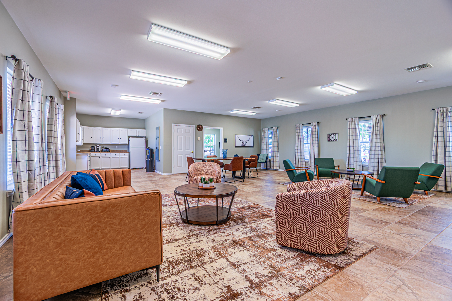 Spacious lounge with sofas, armchairs, coffee tables, and large windows under bright ceiling lights