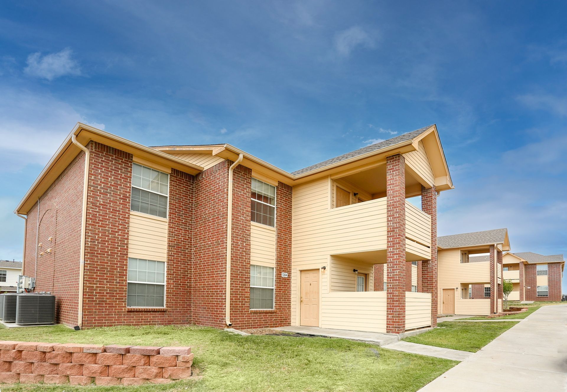 Brick apartment buildings with tan siding and a sidewalk under a blue sky