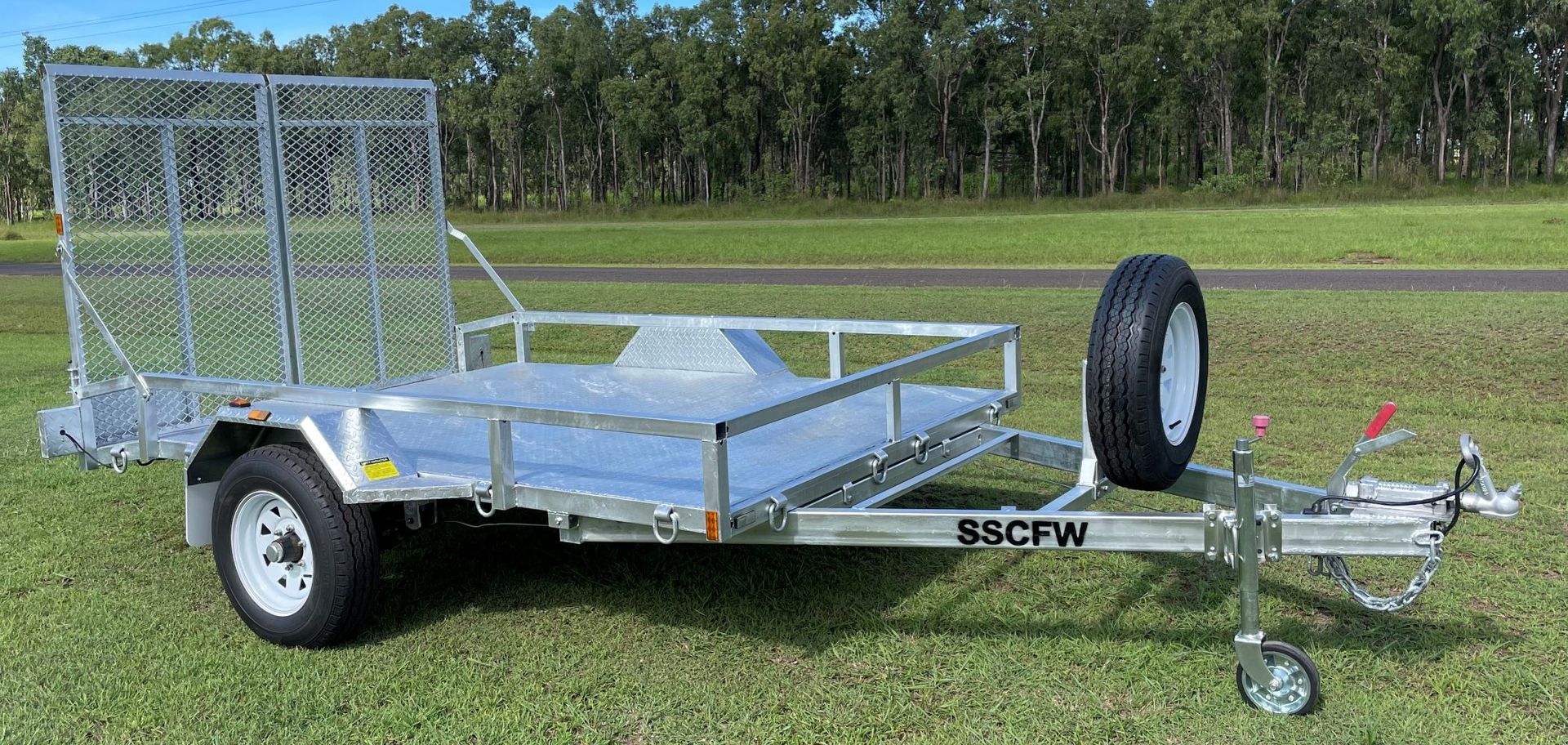 A trailer is parked in a grassy field with trees in the background.