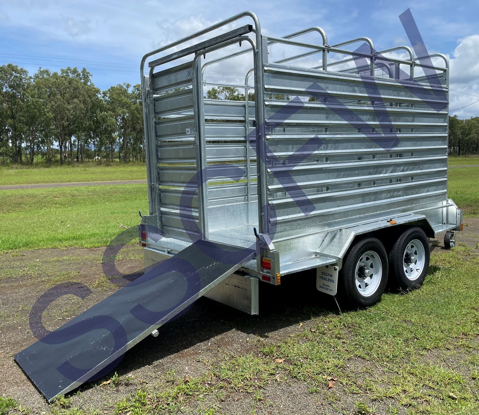 A trailer with a ramp attached to it is parked in a grassy field.