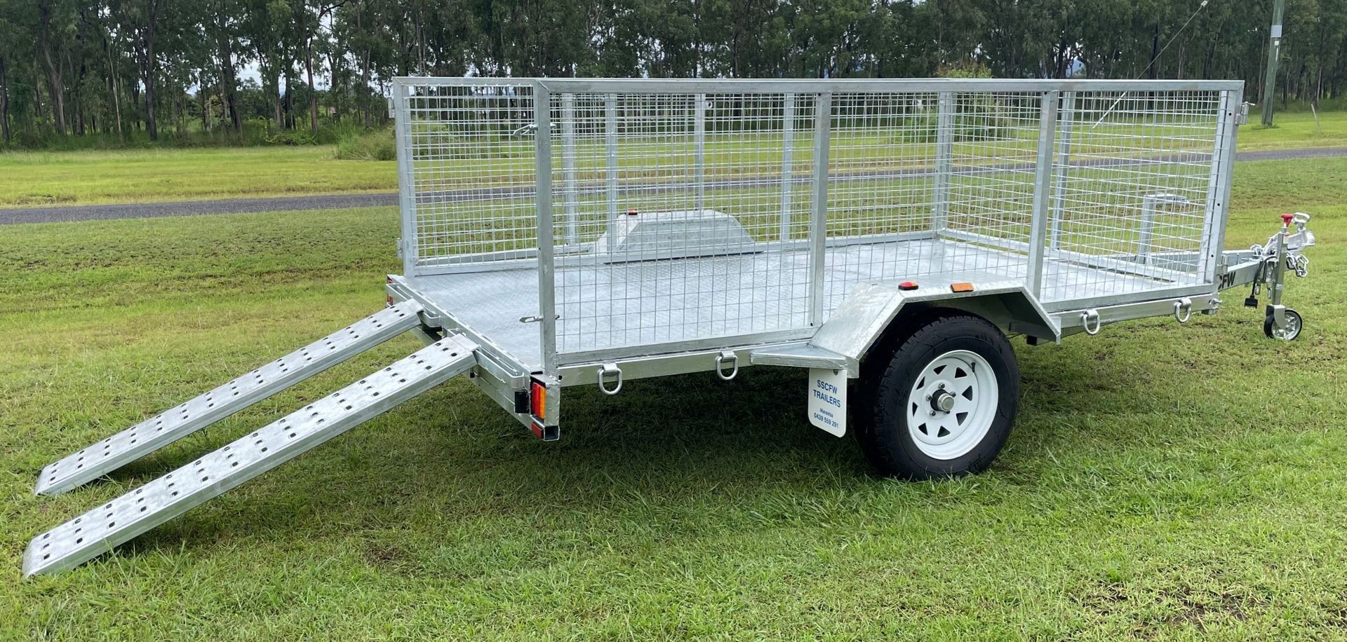 A trailer with ramps attached to it is sitting on top of a lush green field.