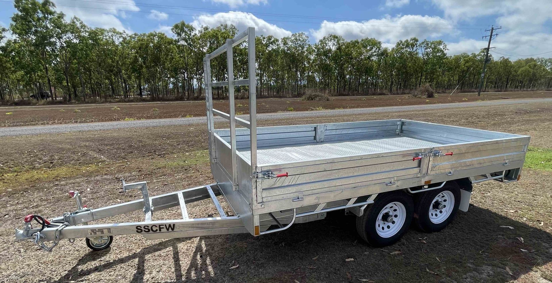 A trailer is parked in a dirt field with trees in the background.