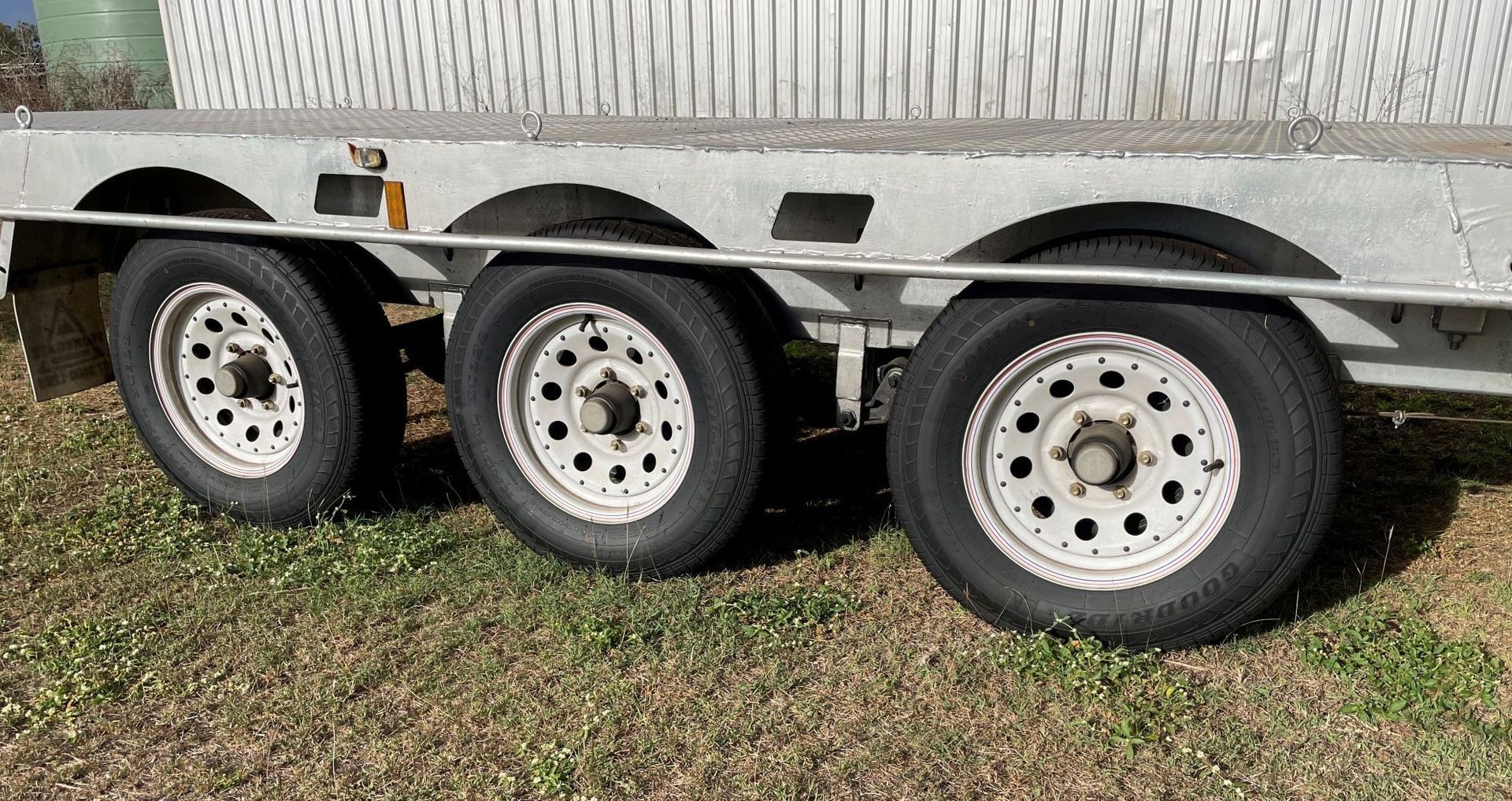 A trailer with three tires is parked in the grass.