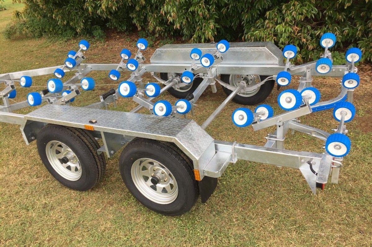 A boat trailer with blue rollers is parked in the grass.