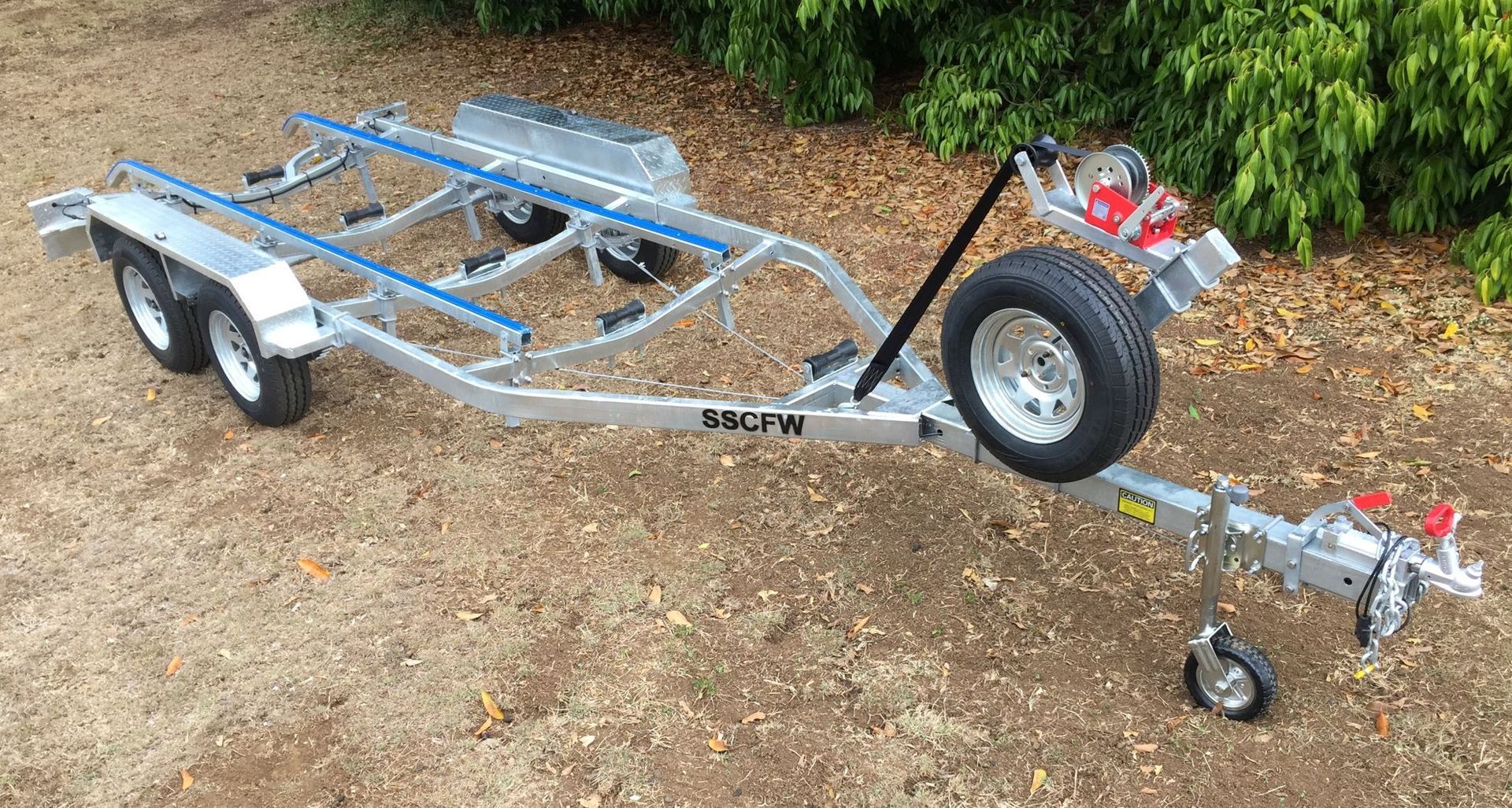 A boat trailer is sitting on the ground next to a bush.