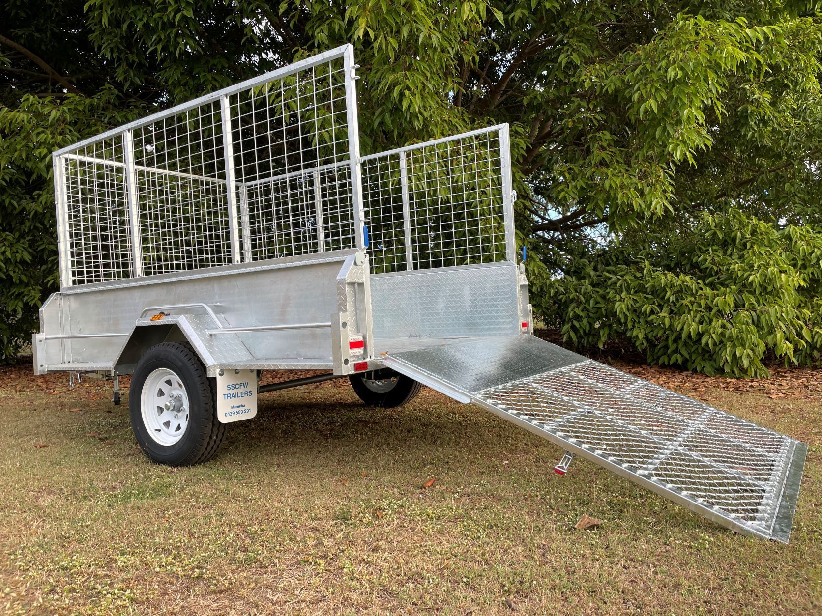 A trailer with a ramp attached to it is parked in the grass.