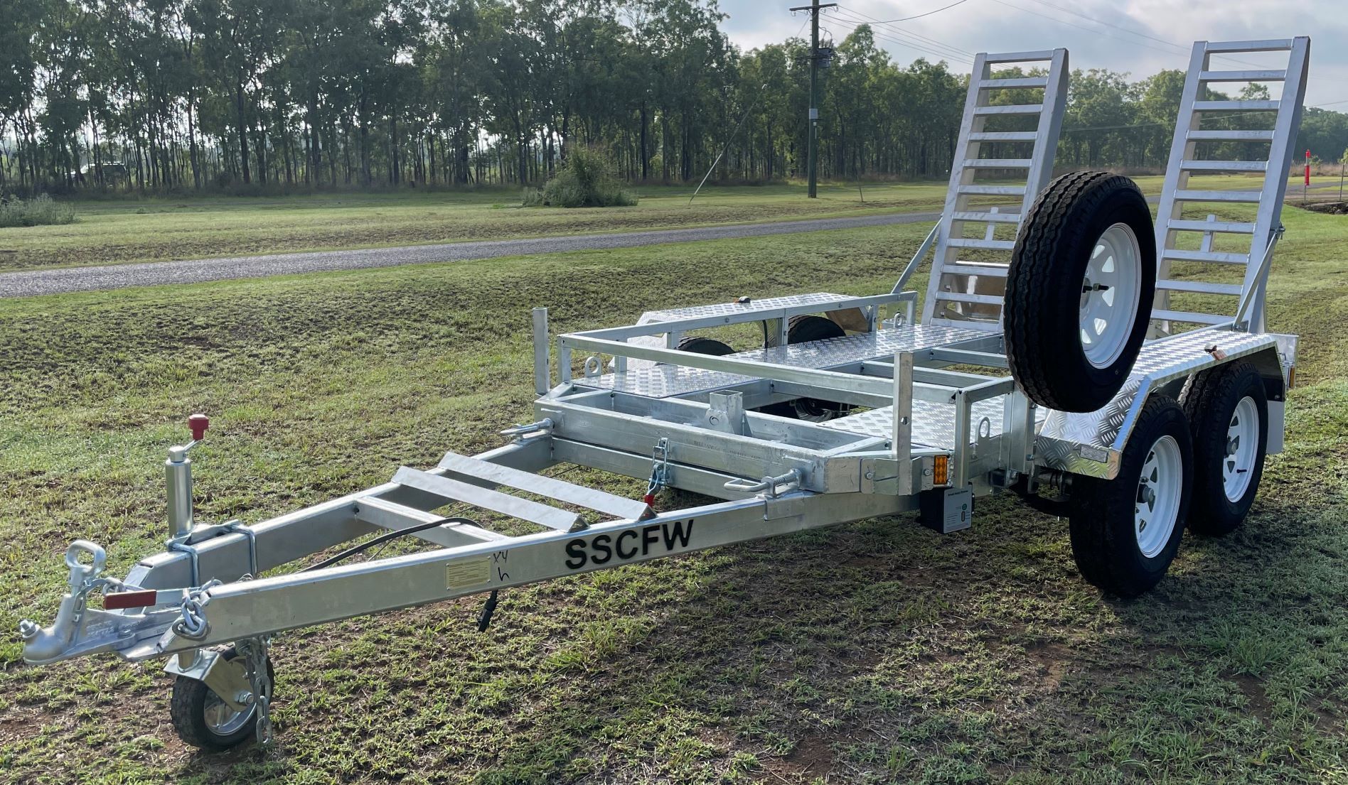 A trailer with two ramps attached to it is parked in the grass.