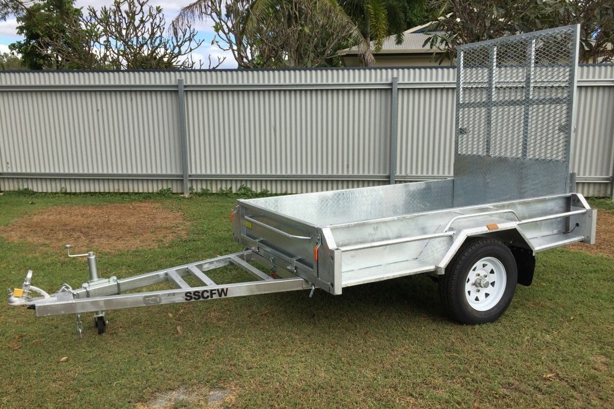A trailer is parked in the grass in front of a fence.