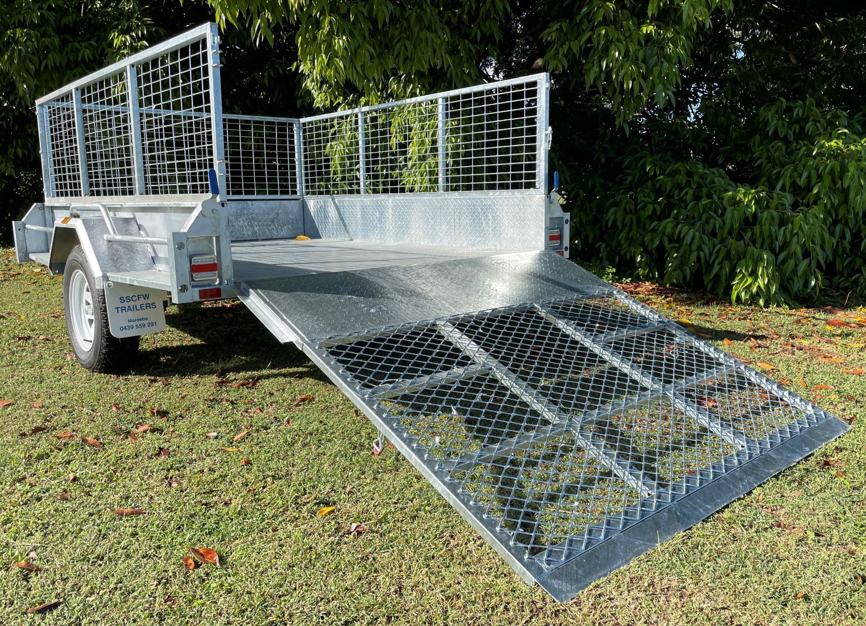 A trailer with a ramp is parked in a grassy field.