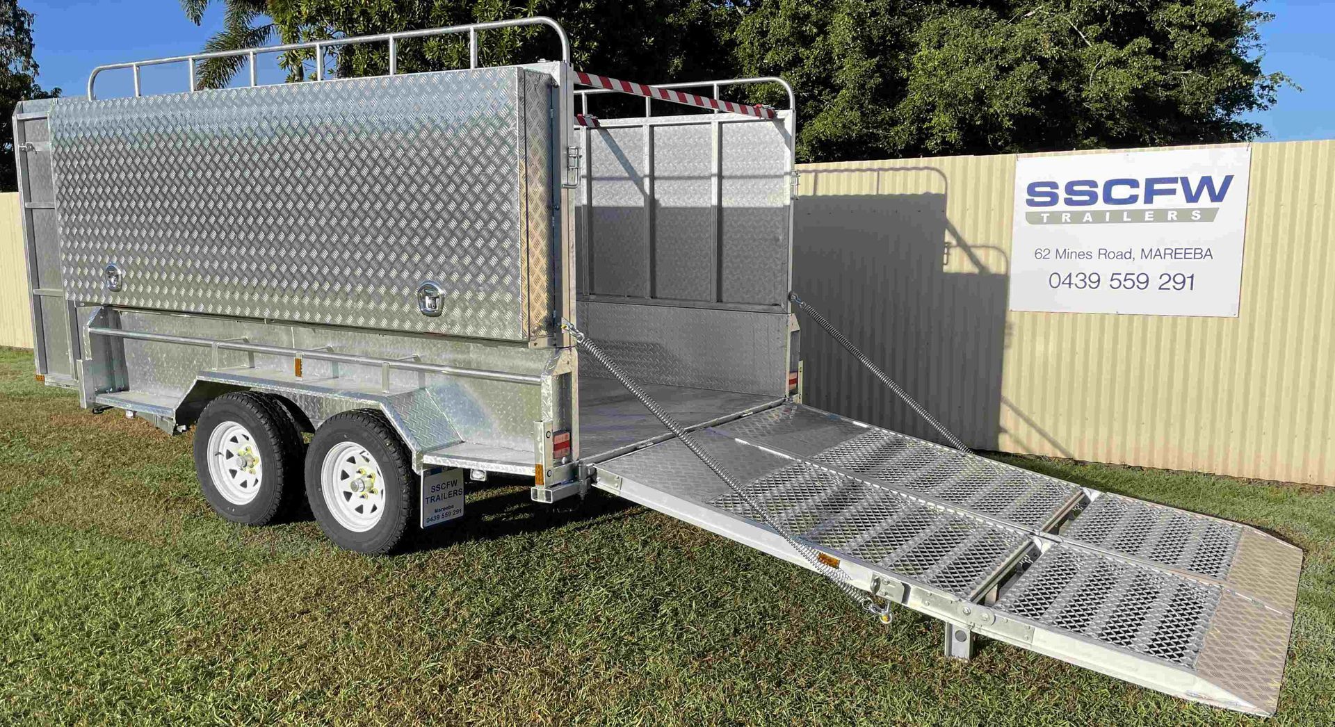 A trailer with two ramps attached to it is parked in the grass.