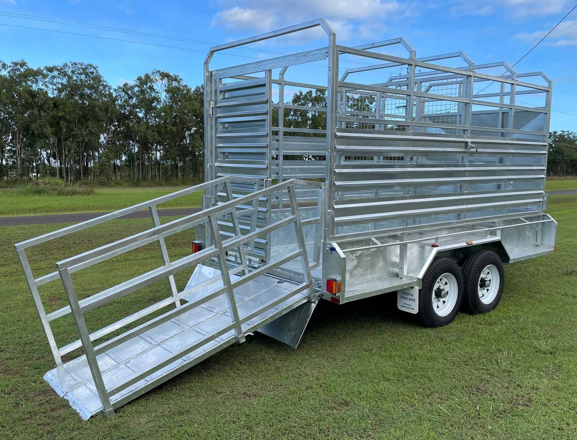 A trailer with a ramp attached to it is parked in a grassy field.