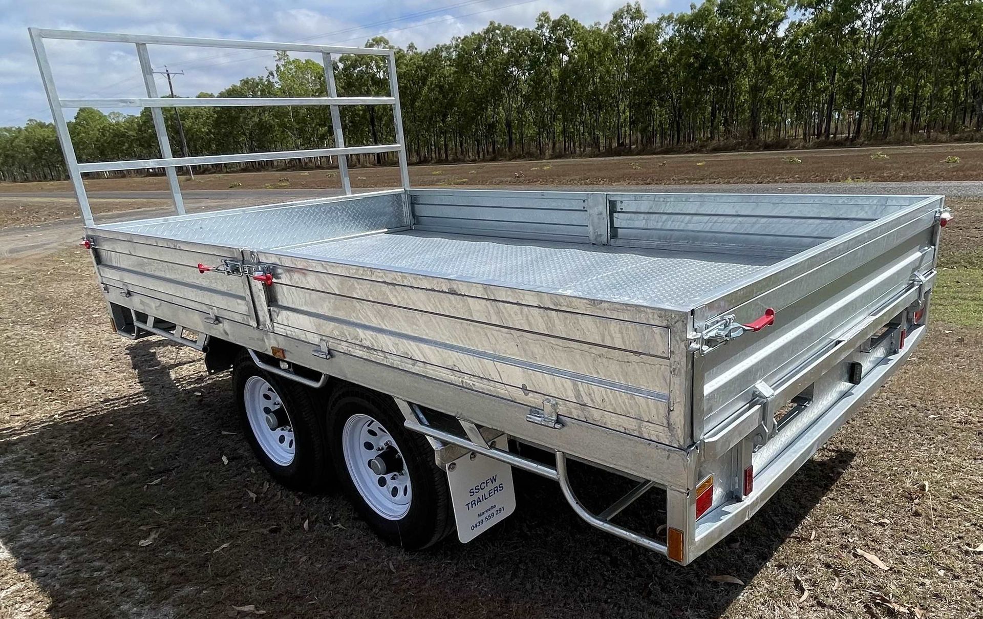 A trailer is parked in a dirt field with trees in the background.