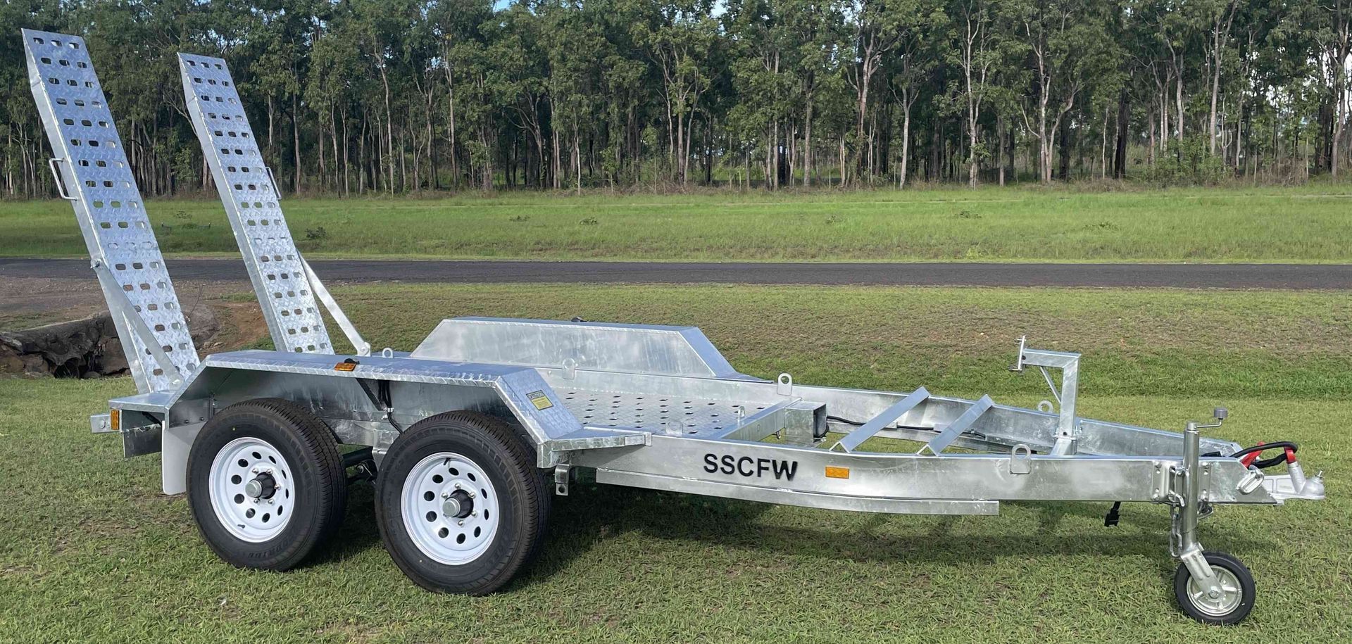 A trailer with two ramps attached to it is parked in the grass.