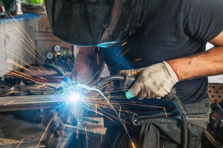 A man is welding a piece of metal in a workshop.