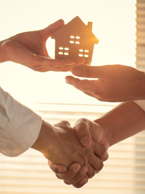 Two people shaking hands beneath a house model symbolizing estate planning and property transfer in Utica, NY.