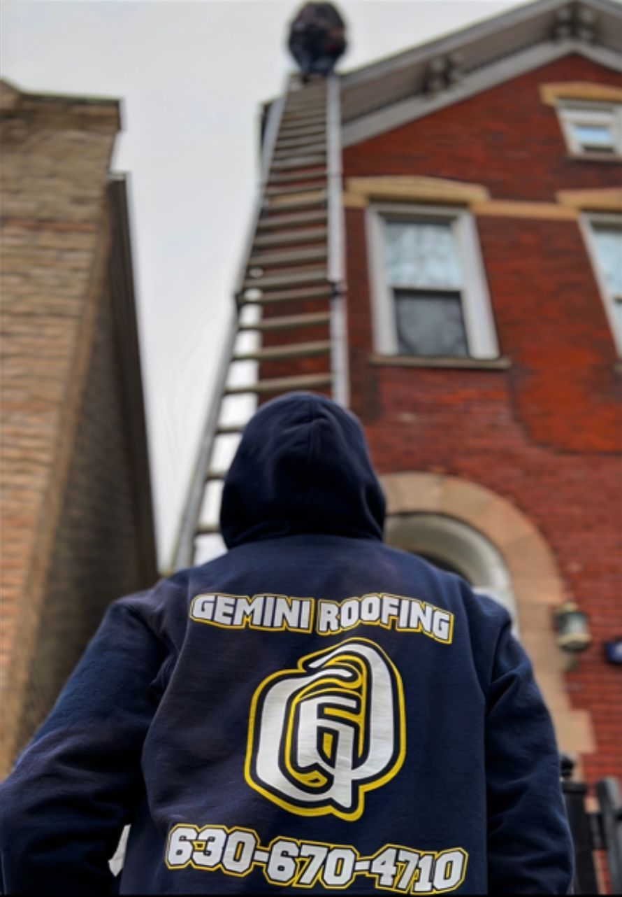 Person in a navy blue Gemini Roofing hoodie watches a worker on a tall ladder ascending to a brick house roof. Sky is overcast.