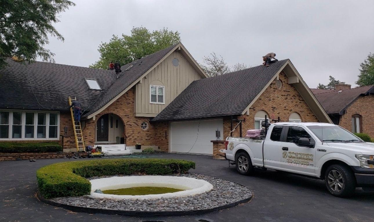 A brick home with a dark roof, a white truck parked in the driveway, and a circular hedge.