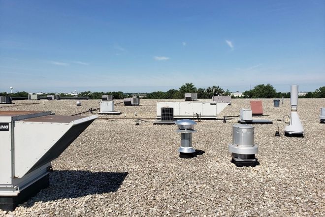 A flat rooftop covered in gravel, with various HVAC units and vents under a clear blue sky.