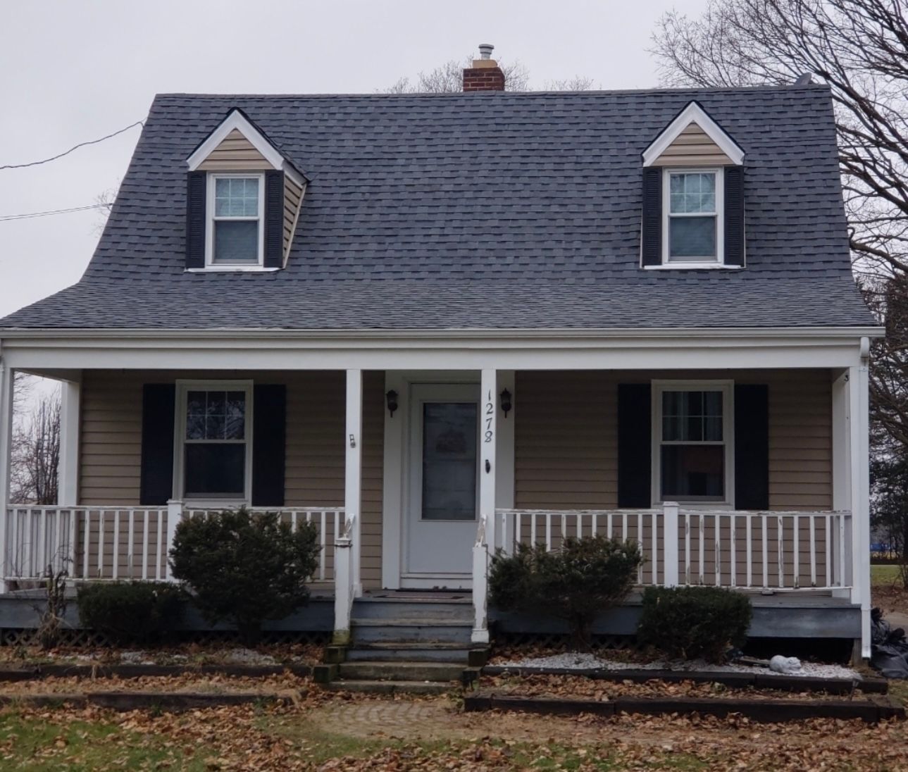 Tan and white Cape Cod house with a porch and a gray roof. Two dormer windows are on the roof.