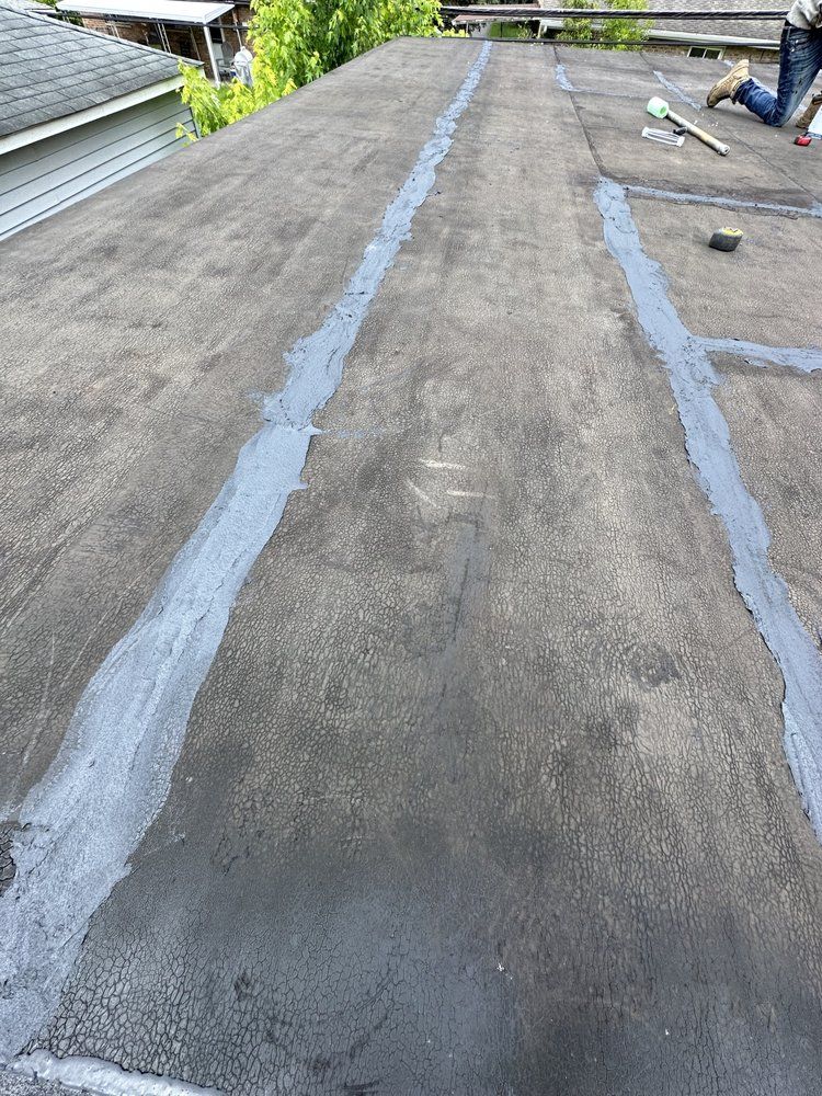 Flat roof with gray sealant applied in lines; a person is visible working on the roof.