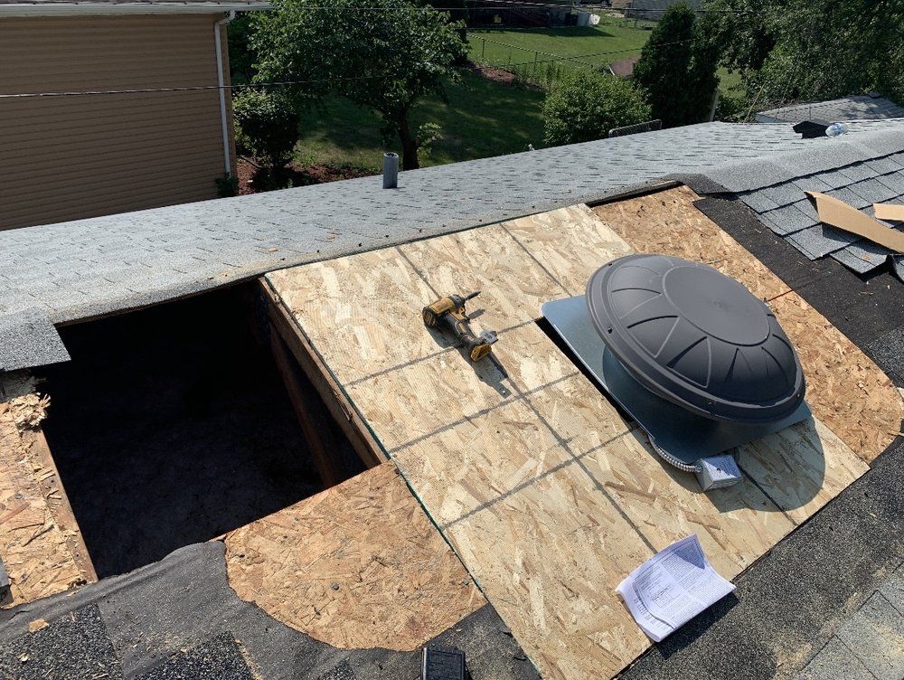 A section of a roof is open, revealing the interior. A vent and plywood are placed on the roof.