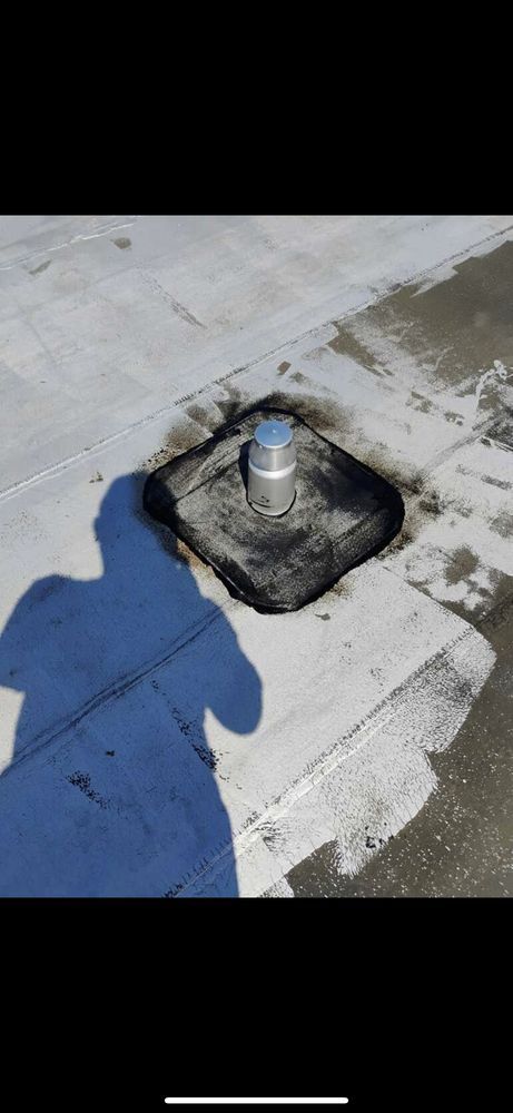 Person applying sealant tape around a roof drain on a flat, black roof. The person is kneeling, holding tape.
