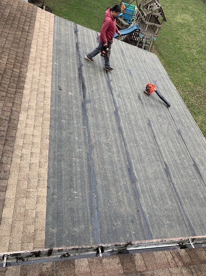 A person works on a roof, using a leaf blower. The roof has new black underlayment and shingles.